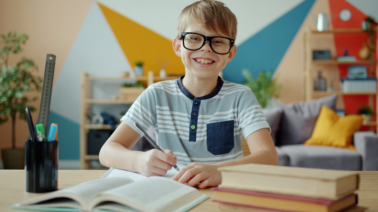 Photo by Vitaly Gariev Smiling boy wearing glasses studying at a desk.